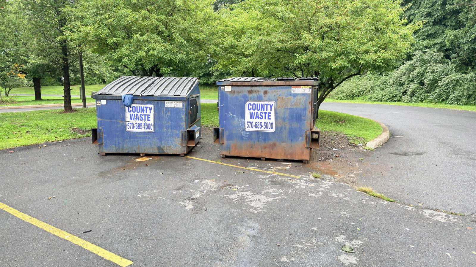 The same dumpster pad swept clear, with clean asphalt around both containers
