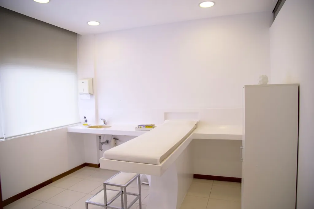 A clean, empty medical exam room with a treatment table, sink and hard-surface flooring
